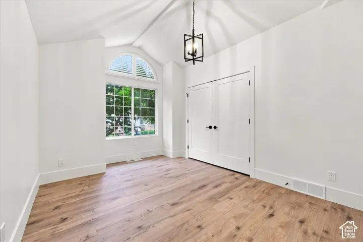 Vaulted ceiling with an exposed beam, wood-finish flooring, arched transom window, white plantation shutters, and a modern chandelier