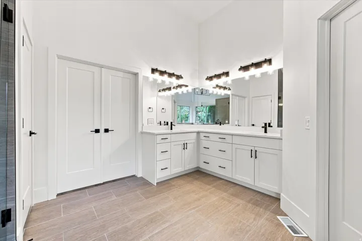 Vaulted ceiling with dual vanity, rectangular undermount sinks, stone countertops, and tile flooring