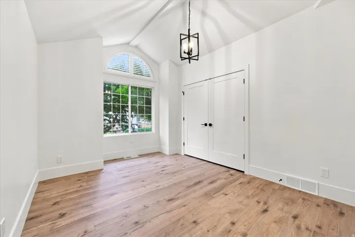Vaulted ceiling with an exposed beam, wood-finish flooring, arched transom window, white plantation shutters, and a modern chandelier