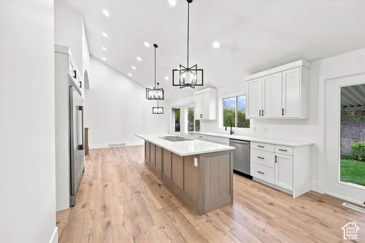 Expansive kitchen featuring a large central island with integrated cooktop, white shaker cabinetry, stainless steel appliances, and wood-finish flooring