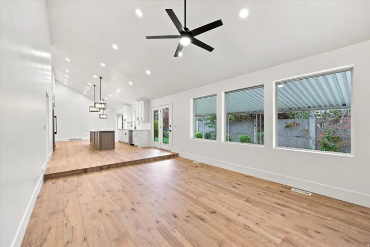 Vaulted ceiling with recessed lighting and a ceiling fan, wood-finish flooring, white walls, and multiple windows