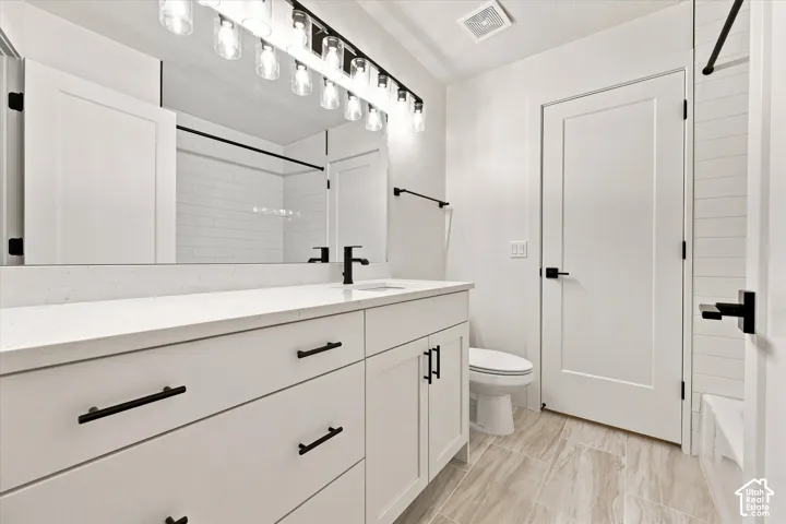 Spacious vanity with a white countertop, modern black fixtures, wood-finish flooring, and subway tile shower surround