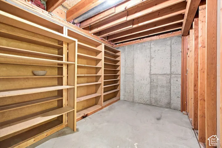Extensive built-in shelving, exposed wood ceiling joists, concrete flooring, and concrete foundation walls