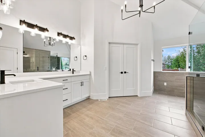 Vaulted ceiling, dual vanity with undermount sinks, quartz countertops, modern black fixtures, and a glass-enclosed shower