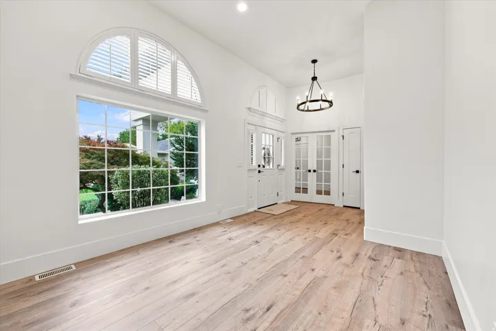 Arched transom window with plantation shutters, large grid-pattern window, wood-finish flooring, double glass-paneled interior doors, and a decorative chandelier