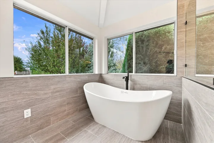 Freestanding bathtub with a floor-mounted matte black faucet, surrounded by large format tile flooring and wainscoting