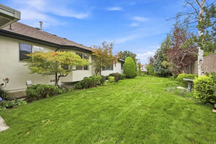 Expansive lawn area with mature landscaping, architectural wall extensions, and a stone bird bath