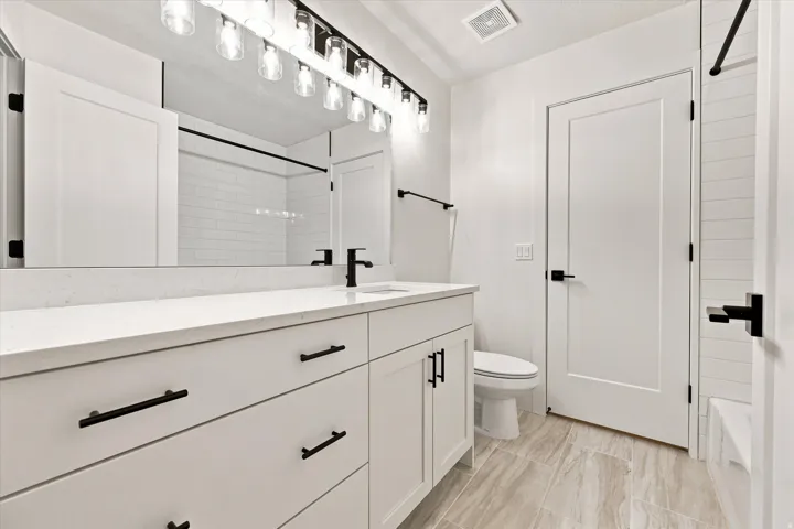 Spacious vanity with a white countertop, modern black fixtures, wood-finish flooring, and subway tile shower surround