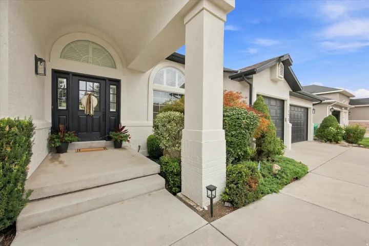 Stucco exterior with a covered entry, dark paneled front door with sidelights, arched transom window, and a two-car garage with dark paneled doors