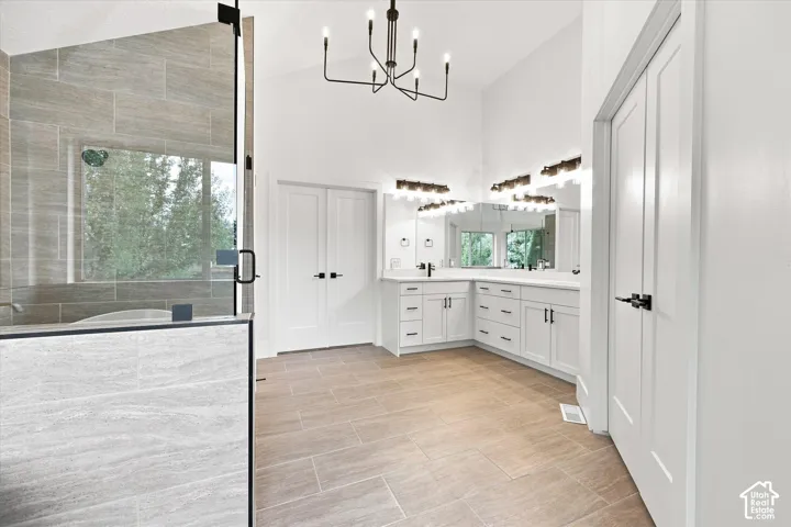 Spacious bath featuring tile flooring, a large glass-enclosed shower, dual vanity with white cabinetry, and contemporary light fixtures