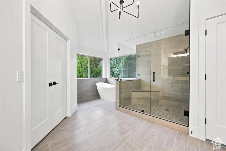 Freestanding tub, glass-enclosed shower with bench, vaulted ceiling, tile flooring, and contemporary chandelier