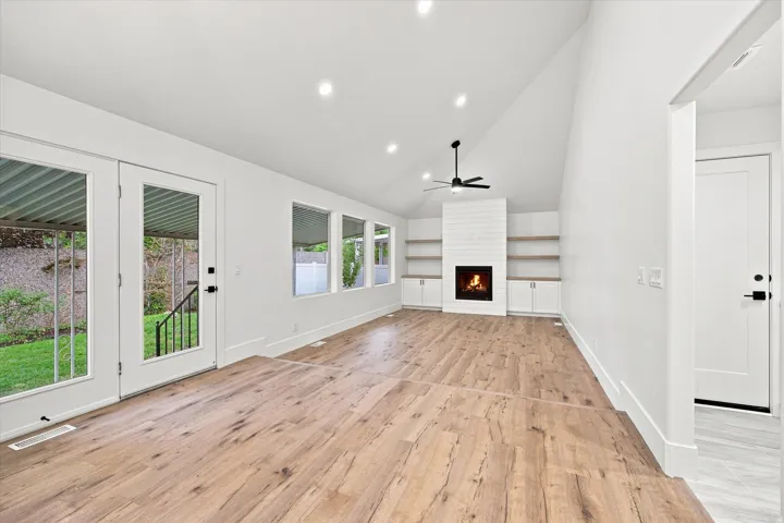Vaulted ceiling living area featuring wood-finish flooring, a contemporary fireplace with shiplap surround, and built-in shelving