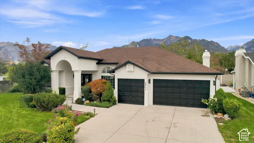 Stucco exterior with an arched entry, two-car garage with black doors, manicured lawn, and mature landscaping