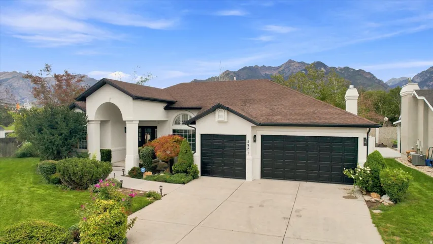 Stucco exterior with an arched entry, two-car garage with black doors, manicured lawn, and mature landscaping