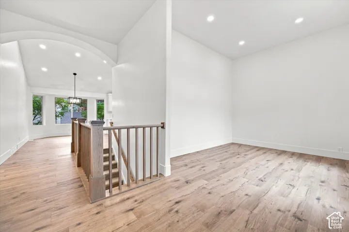 Recessed lighting, wood-finish flooring, staircase with wood railing, arched ceiling detail, and large window openings
