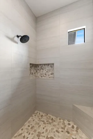 Walk-in shower featuring large format wall tiles, a built-in bench, and a tiled shower niche