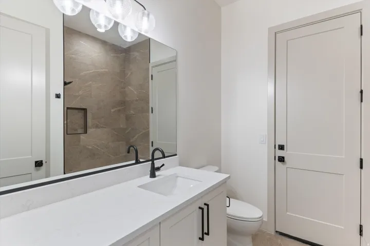 Vanity with a white countertop and integrated sink, matte black fixtures, and light wood-finish cabinetry