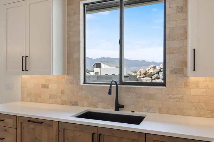White upper cabinetry, wood-finish lower cabinetry, light-toned backsplash, white countertop, and black basin sink with matching faucet