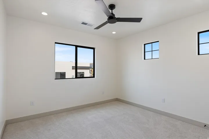 White walls, recessed lighting, ceiling fan, black-framed windows, and light-colored carpeting