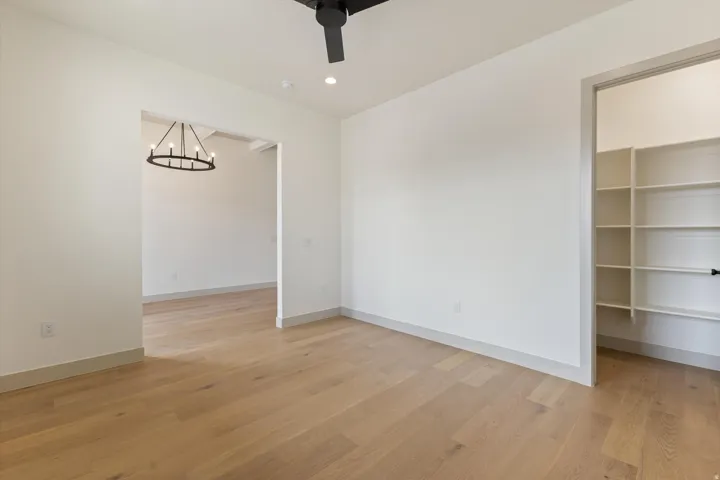 Light wood-finish flooring, recessed lighting, and a black ceiling fan, with an archway revealing a black chandelier