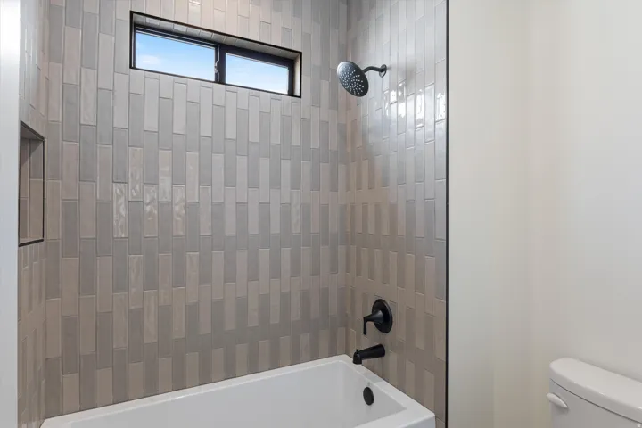 Bathtub with a tiled surround, matte black fixtures, an integrated shower niche, and a transom window