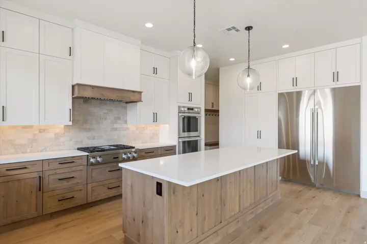 Spacious kitchen featuring white upper cabinetry, wood-finish lower cabinetry, stone countertops, and stainless steel appliances