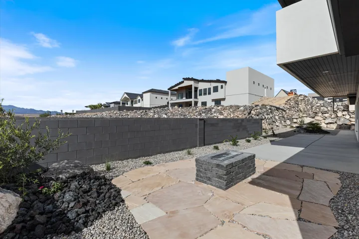 Outdoor living space featuring a paver patio with a built-in fire pit, concrete block retaining wall, and aggregate rock landscaping