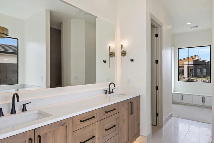 Dual vanity featuring wood-finish cabinetry, white countertops, and matte black fixtures