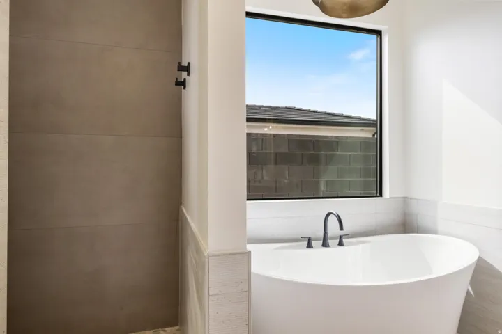 Freestanding soaking tub with matte black fixtures, large window, and tiled shower surround