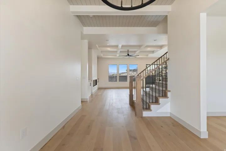 Wood-finish flooring throughout, coffered ceiling, and a staircase with wood newel posts and black iron balusters