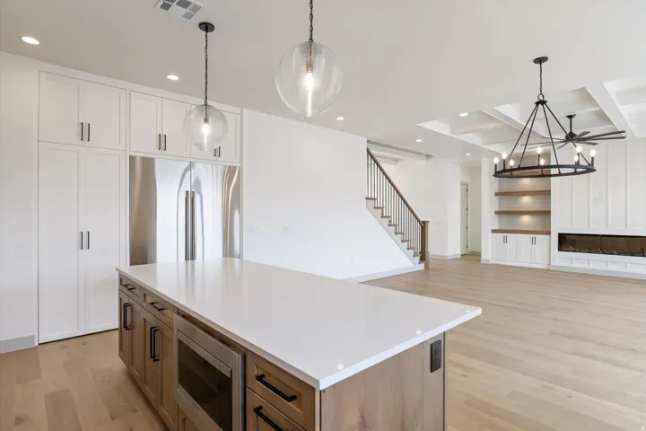 Kitchen island with a light-toned countertop, stainless steel appliances, wood-finish flooring, a contemporary fireplace, and a coffered ceiling
