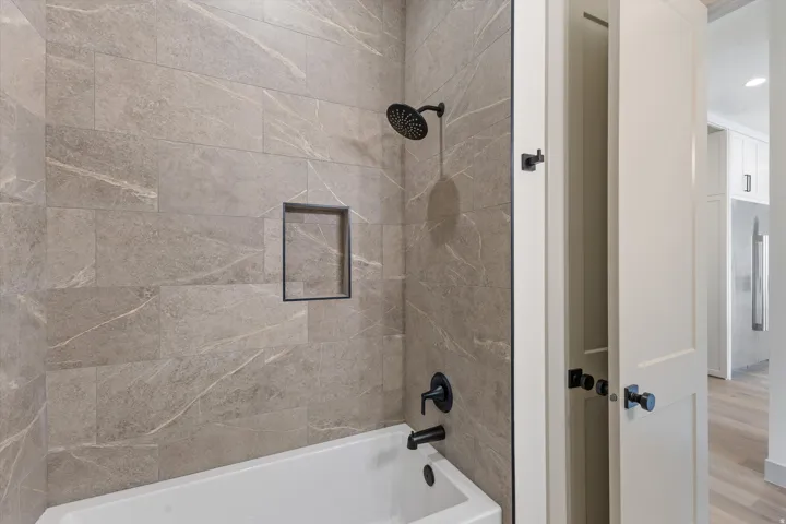 Bathtub with integrated shower, dark bronze fixtures, and a recessed tiled niche