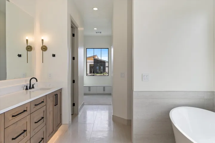 Freestanding bathtub, wood-finish vanity with countertop, rectangular undermount sink, matte black faucet, and brass wall sconces