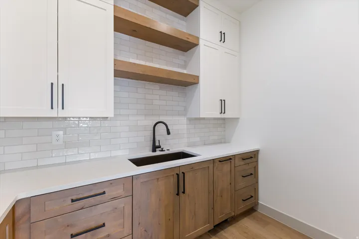 White shaker-style cabinetry, wood-finish base cabinetry, white subway tile backsplash, solid surface countertop, and wood-finish open shelving