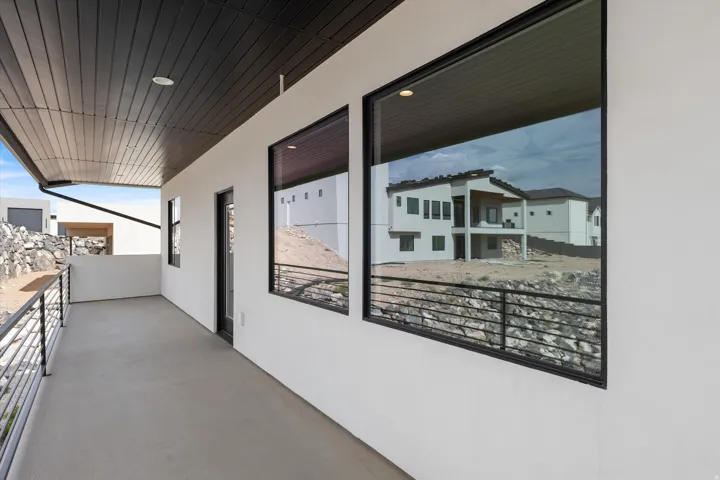 Covered concrete balcony with recessed lighting, black railing, and black-framed windows