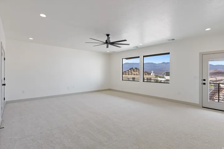 Spacious room with carpeted flooring, a ceiling fan, recessed lighting, two large windows, and an exterior door with glass panels