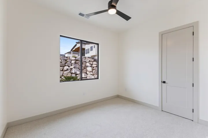 Neutral tone walls and carpeting, a contemporary ceiling fan with integrated lighting, a rectangular window, and a panel door with dark hardware