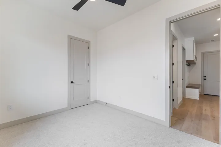 Light grey carpeting, contemporary ceiling fan, grey interior door, and light wood-finish flooring in the adjacent area