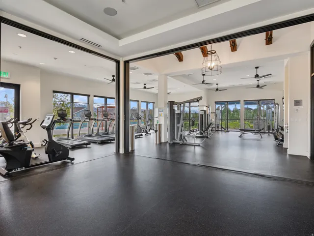 Spacious fitness center featuring rubber flooring, large windows, and exposed ceiling beams