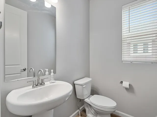 Pedestal sink with a brushed nickel faucet, large wall mirror, and modern light fixture