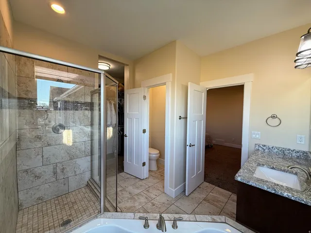 Glass-enclosed shower with tile surround and accent band, corner soaking tub, and vanity with integrated sink and stone countertop