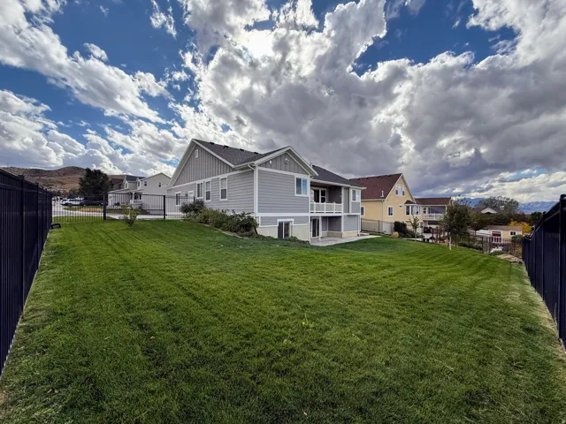 Expansive lawn with a black metal fence, two-story exterior with siding, and a covered patio