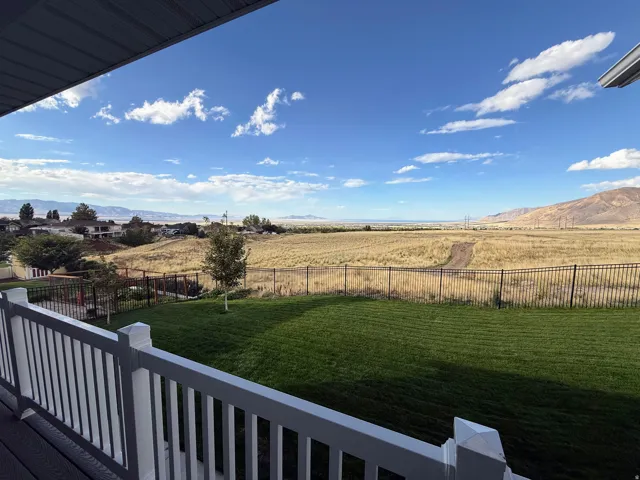 Expansive backyard with manicured lawn, framed by a black metal fence, overlooking open fields and distant mountains