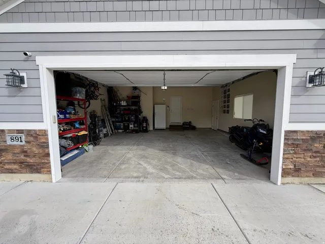 Attached two-car garage with concrete flooring, interior window, and two exterior sconces