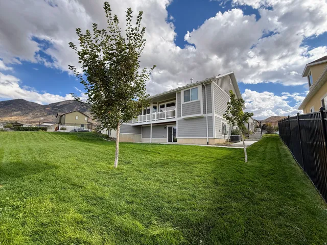 Spacious backyard with a vibrant lawn, mature tree, and a two-story exterior featuring a balcony with white railing