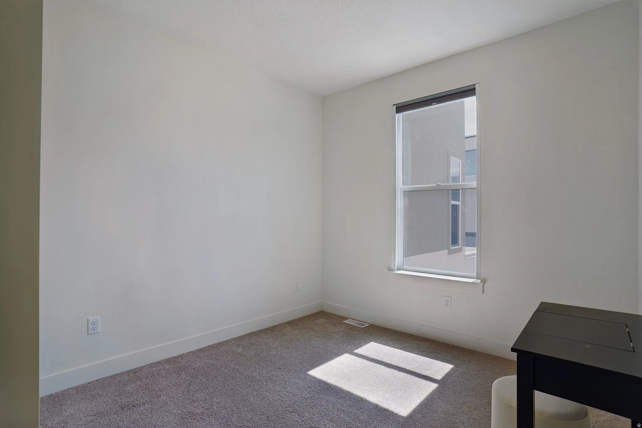 Carpeted flooring, white walls, and a single window with a roller shade