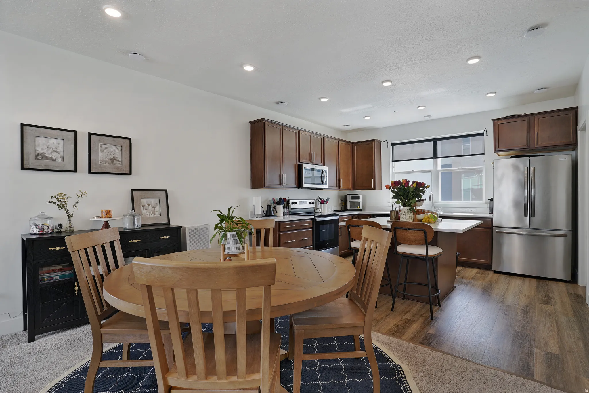Open concept kitchen featuring wood-finish flooring, stainless steel appliances, dark wood cabinetry, a center island with seating, and recessed lighting