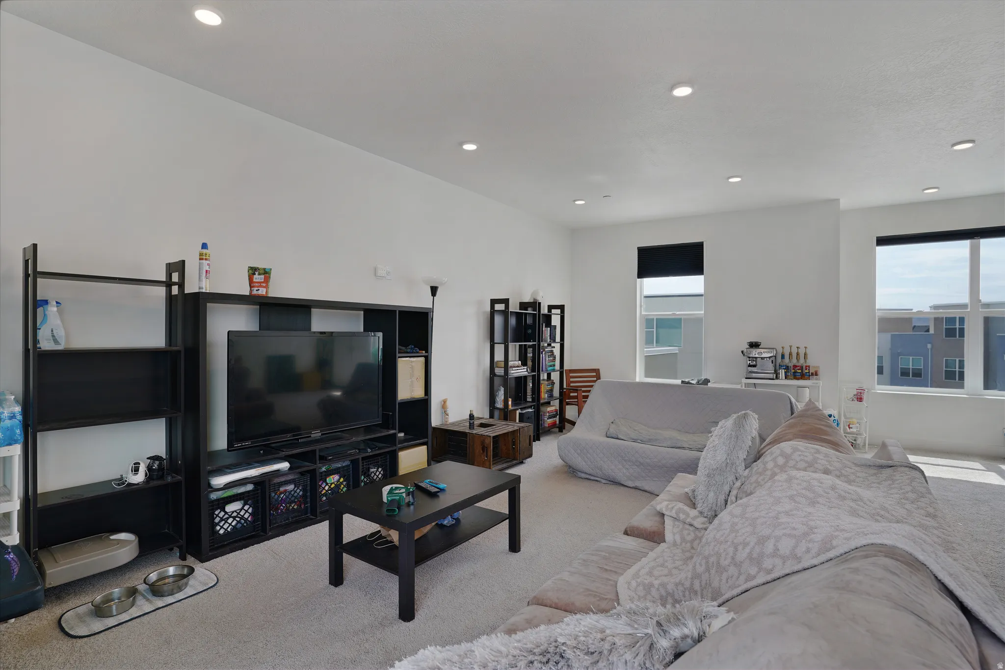 White walls with recessed lighting, multiple windows with roller shades, and light-toned carpeting