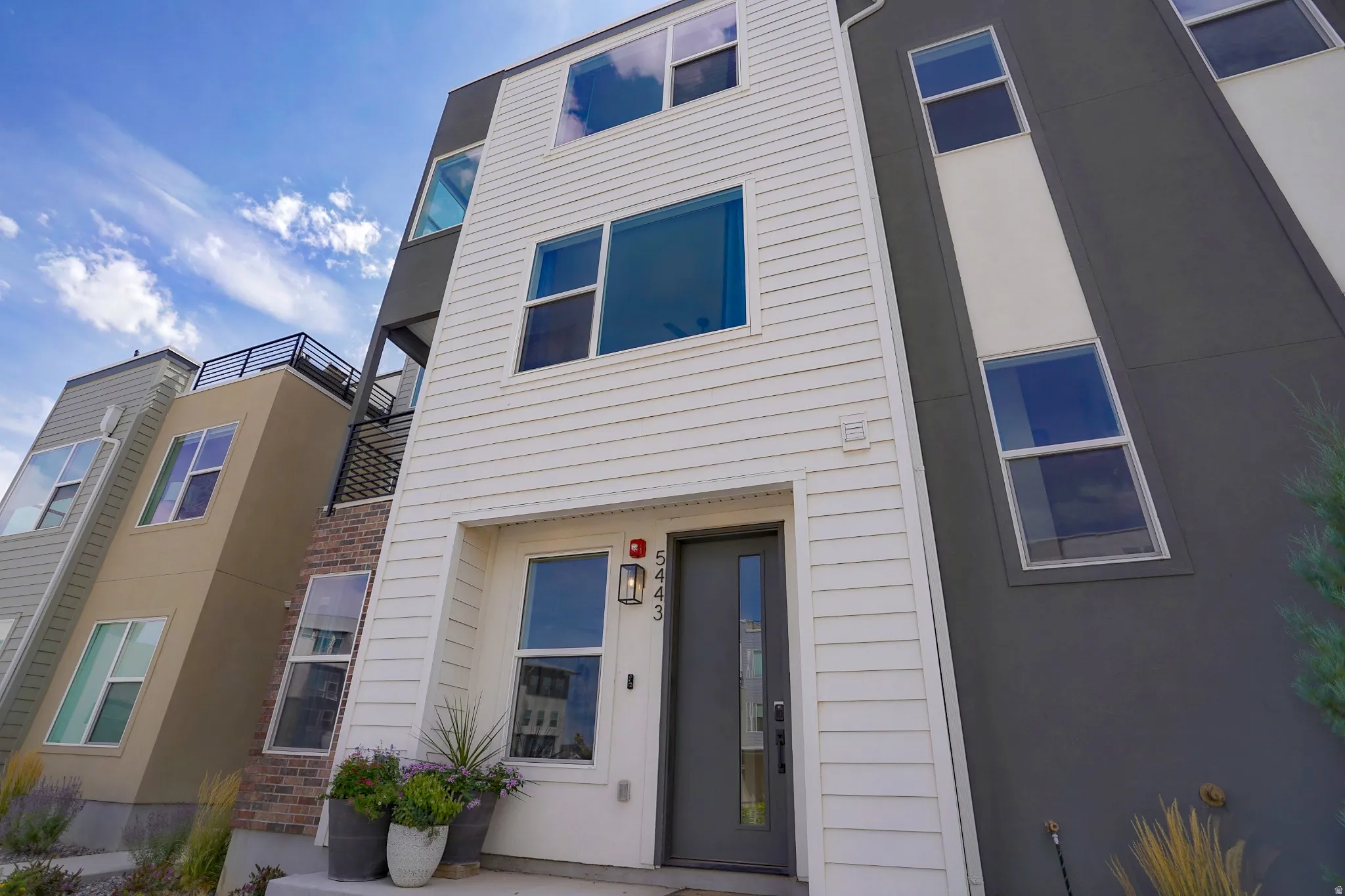 Modern exterior with white horizontal siding, dark gray and white accent panels, multiple large windows, and a black entry door with a glass insert