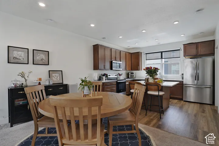 Open concept kitchen featuring wood-finish flooring, stainless steel appliances, dark wood cabinetry, a center island with seating, and recessed lighting